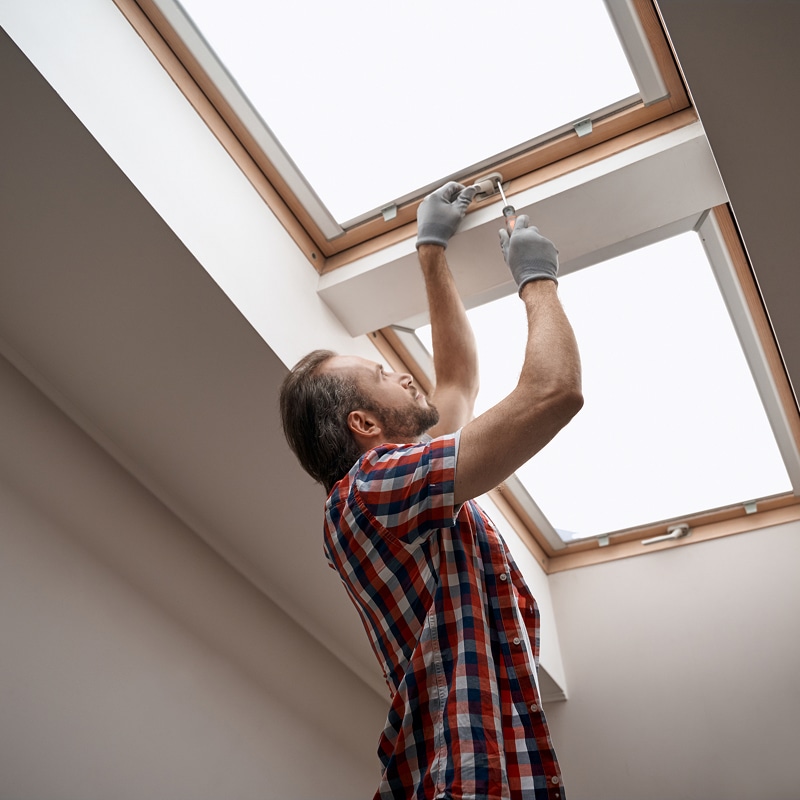 Un homme en gants répare une fenêtre de toit Velux avec un tournevis.
