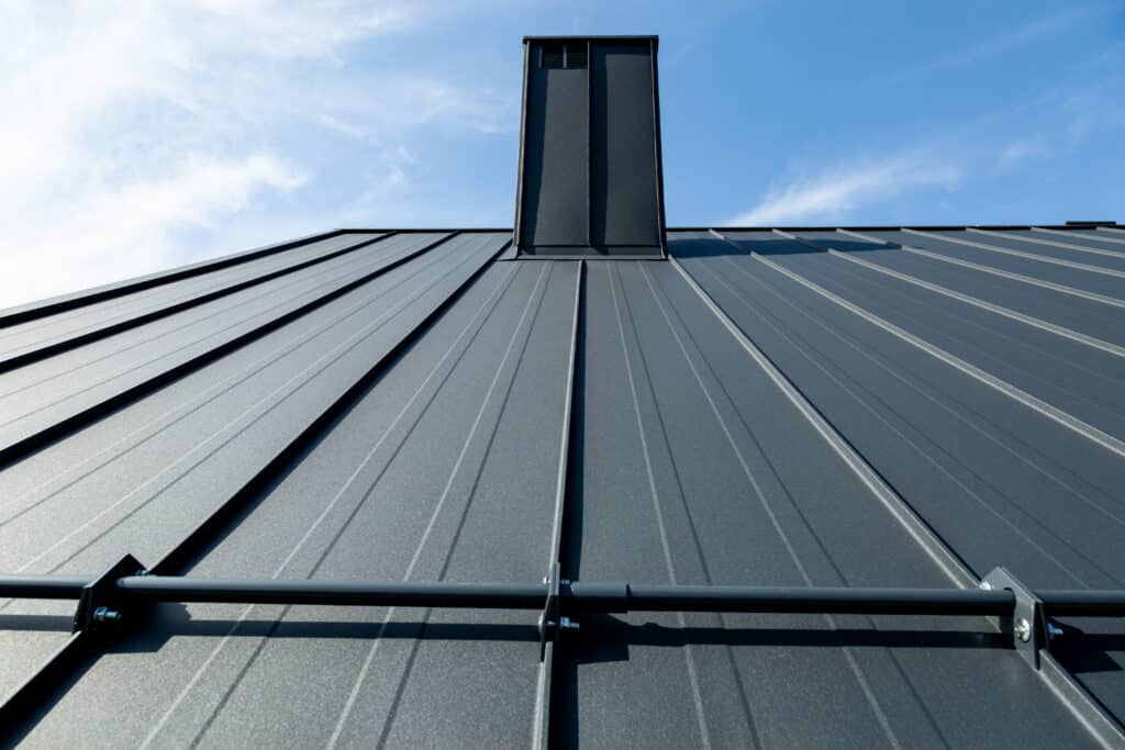 Toit métallique gris anthracite moderne avec cheminée et barre de rétention, sous un ciel bleu clair.